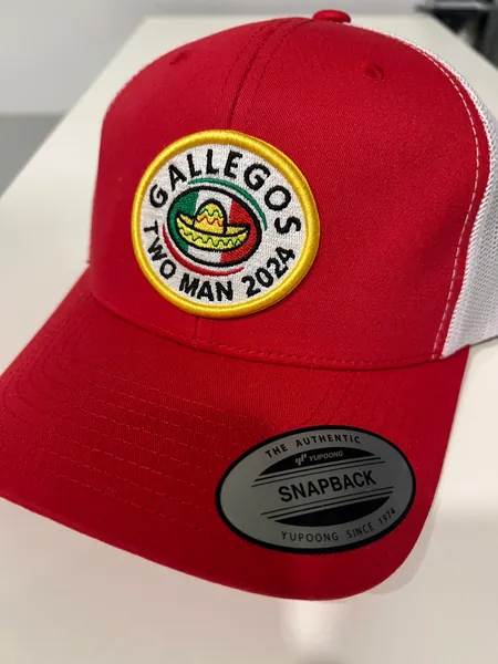 Red and white trucker cap with a round Gallegos Two Man 2024 embroidered patch