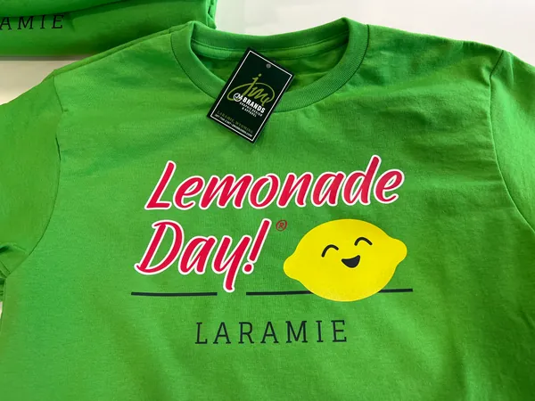 Green tee with a Lemonade Day! Laramie design and a smiling lemon, with a JM4 Brands hang tag
