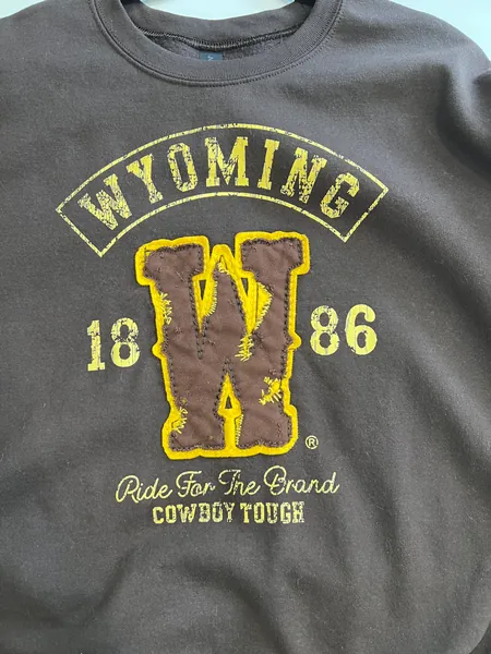 Brown crewneck printed with Wyoming 1886, Ride For The Brand and Cowboy Tough around a distressed appliqué W